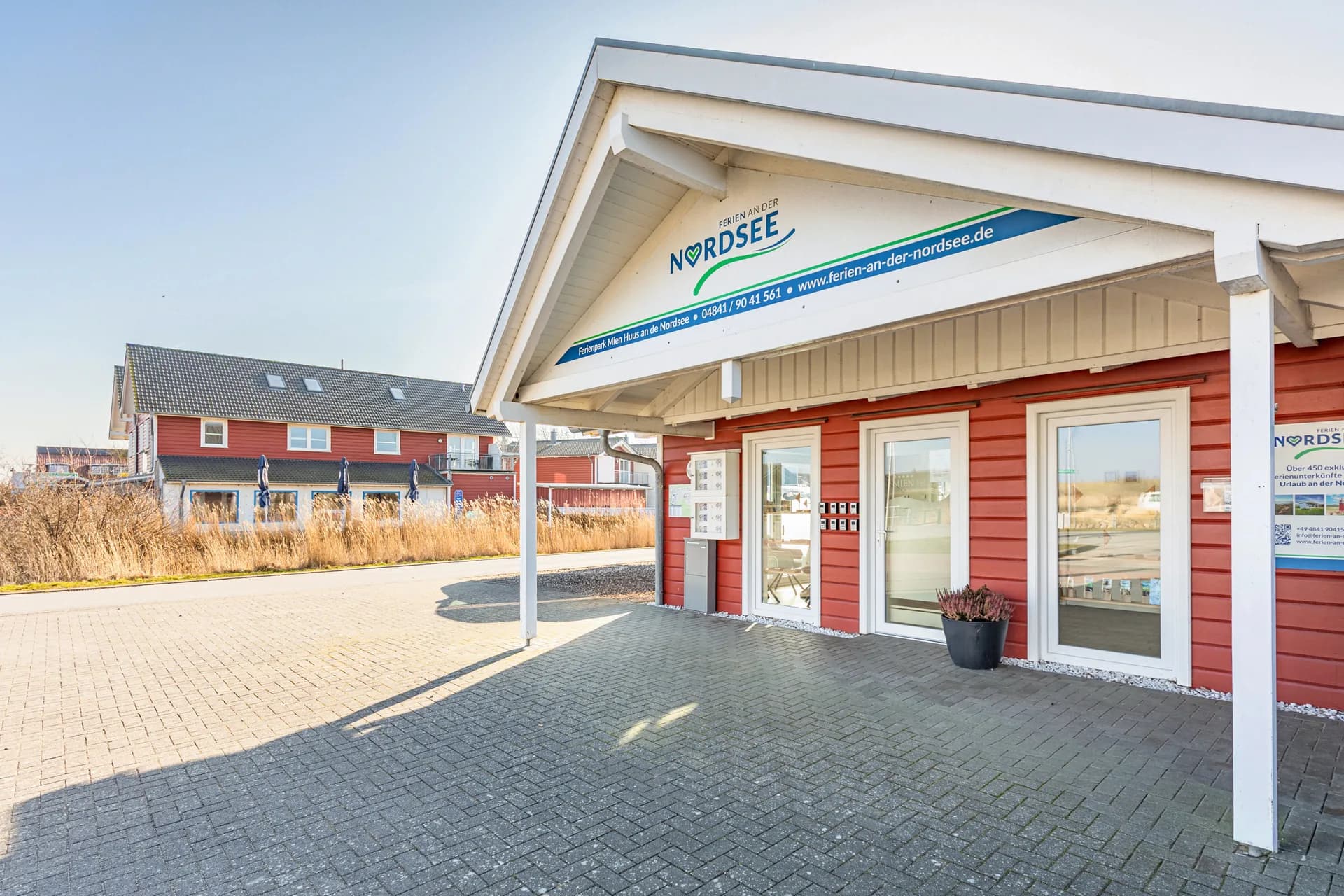 Servicebüro von Ferien an der Nordsee in Dagebüll, rotes Holzhaus mit überdachtem Eingang am Ferienpark Mien Huus an de Nordsee