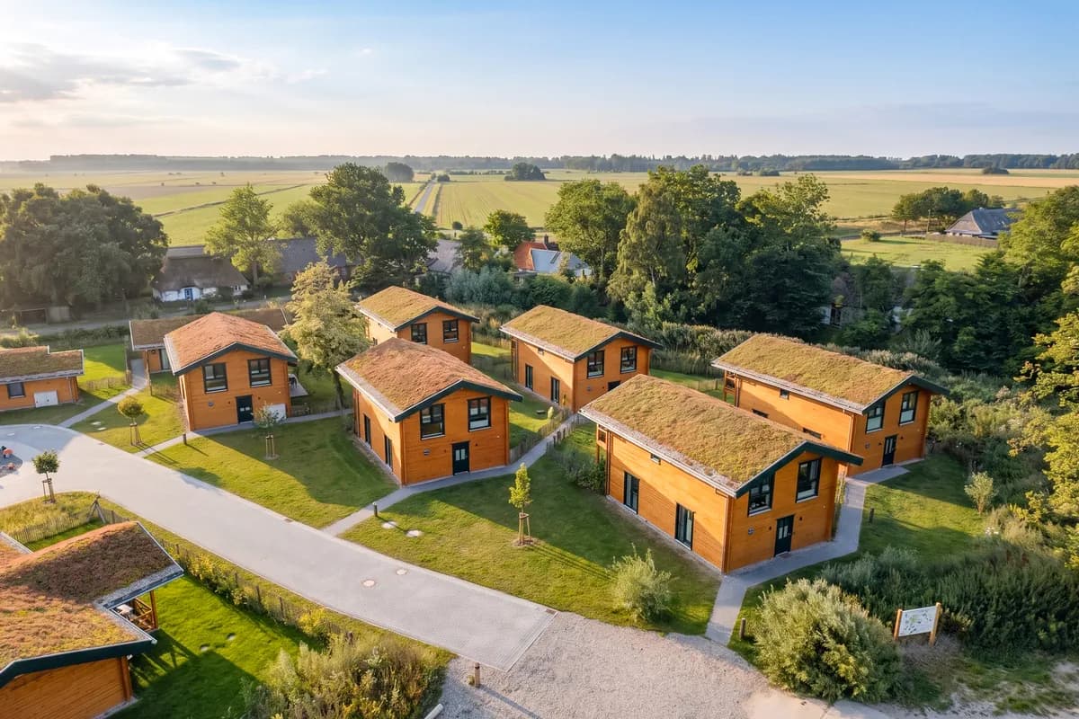 Große Ferienhäuser vom Haustyp Wald auf der WattWarft mit begrüntem Dach und Holzfassade, dahinter Felder auf Eiderstedt