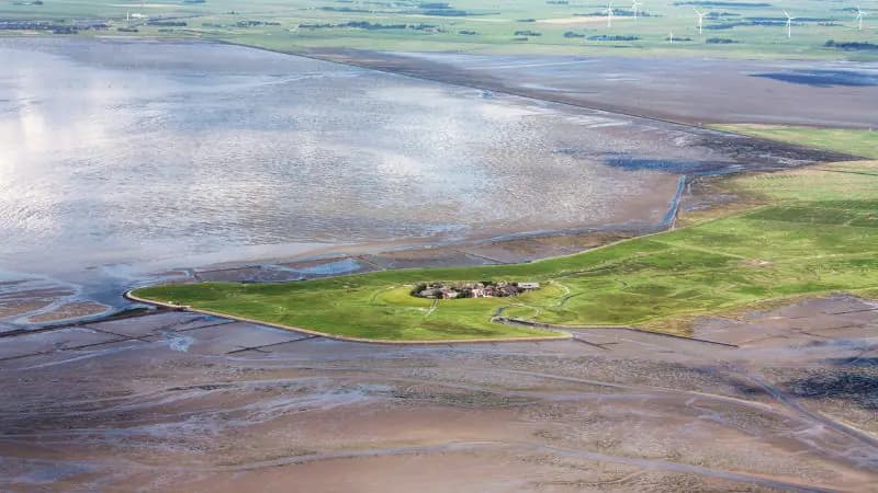 Die Hallig Oland aus der Luft: eine Warft und der schmale Damm der Lorenbahn zum Festland