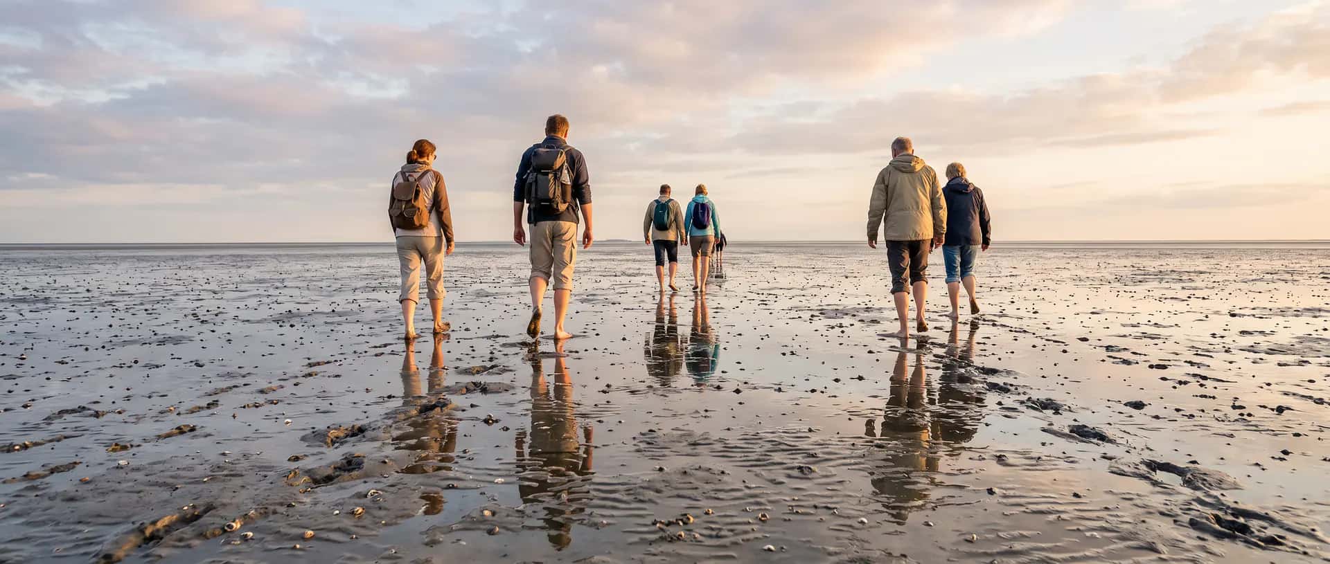 Geführte Wattwanderung in Nordfriesland: Gruppe läuft bei Ebbe barfuß durch das Watt Richtung Horizont